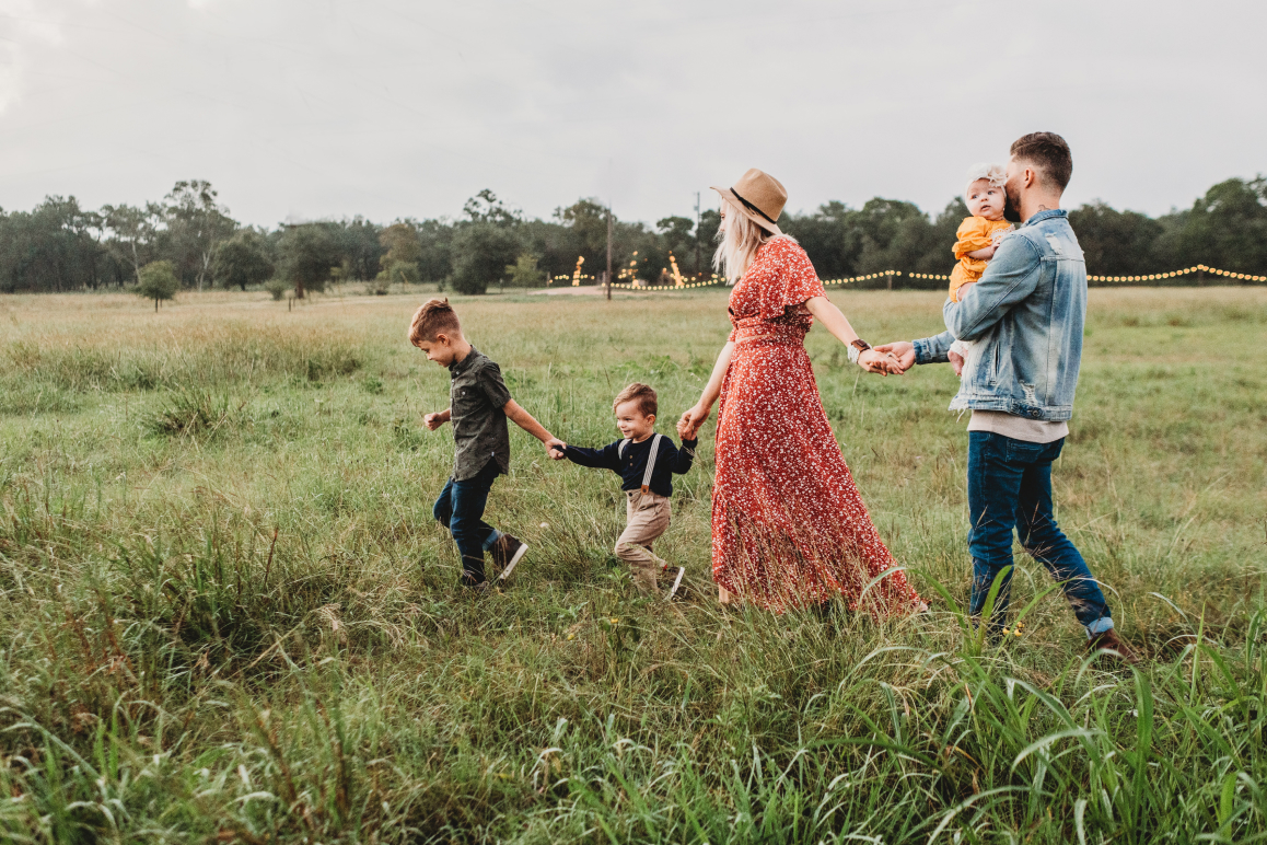 Eine Familie mit drei Kindern, die durch hohes Gras geht.