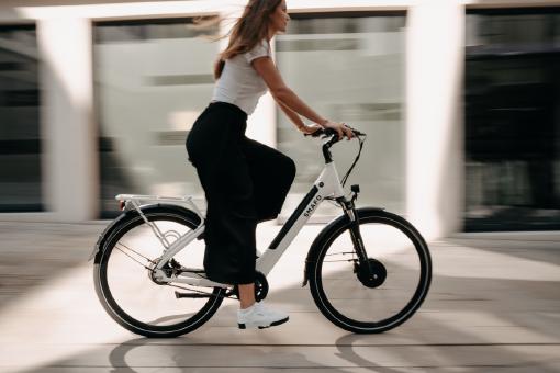 Eine Frau, die ein weißes E-Bike fährt, dass über eine E-Bike Versicherung versichert ist.