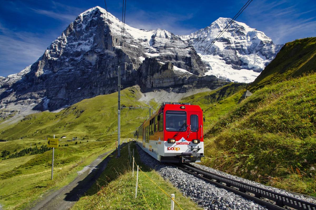 Roter Pendlerzug vor schneebedeckten Alpen. Ein Symbolbild für die private Krankenversicherung für Grenzgänger zwischen Österreich und Schweiz/Liechtenstein.