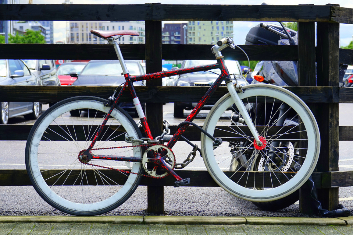 Ein rotes Fahrrad, das mit einem Schloss an einem Geländer befestigt ist.