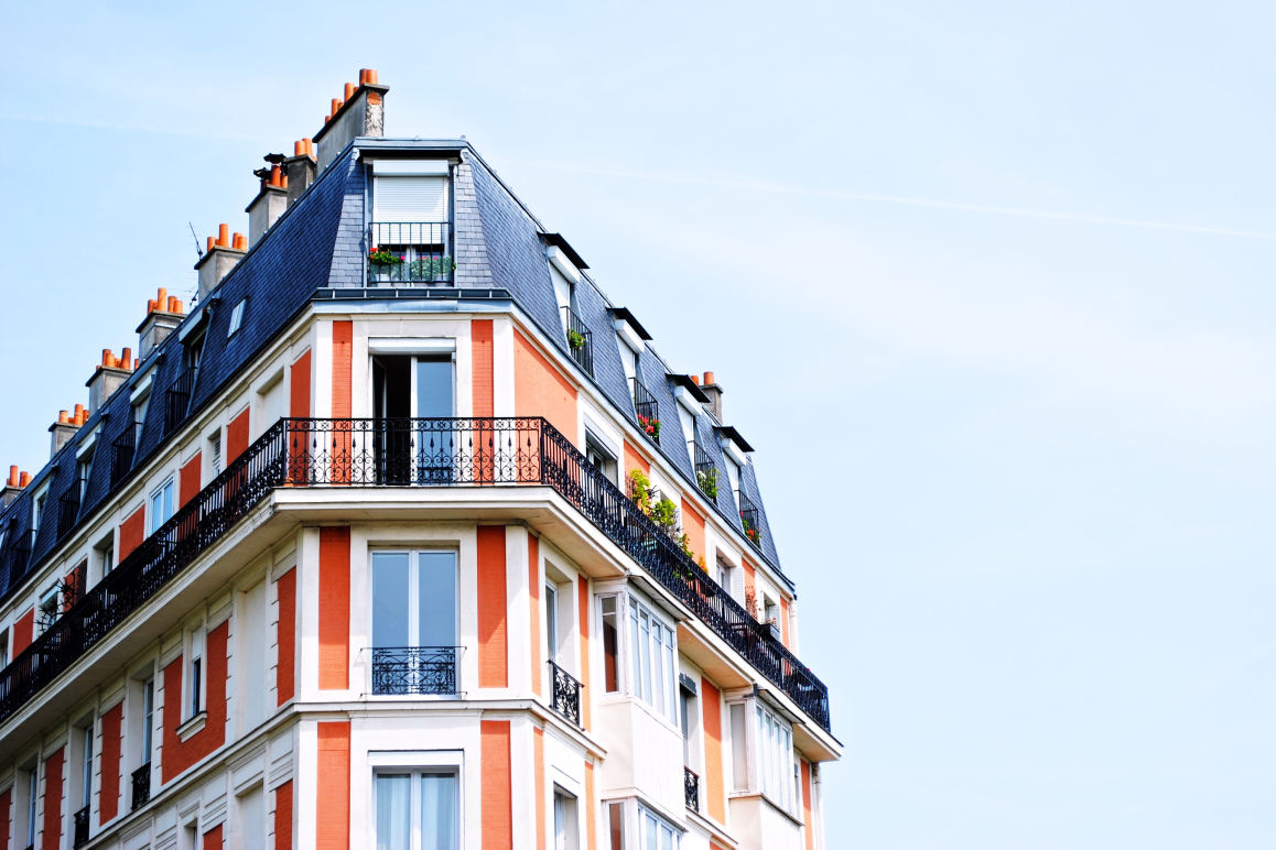 Ein renoviertes Altbau-Mehrparteienhaus vor blauem Himmel mit geöffneter Balkontür.