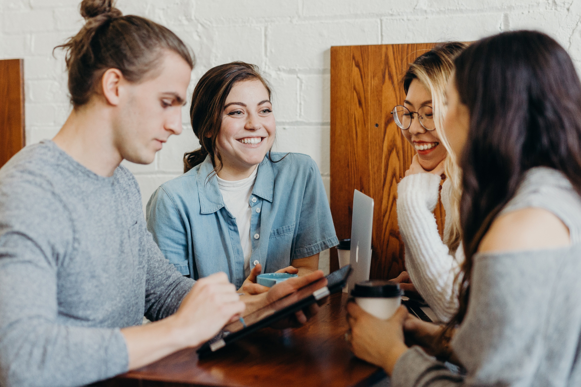 Vier junge Menschen sitzen an einem Tisch und unterhalten sich über Haushaltsversicherungen, dabei lachen sie und scheinen viel Freude zu haben.