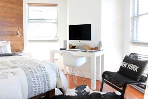 Modern eingerichtetes Schlafzimmer mit weißem Arbeitsplatz, iMac, stilvollen Deko-Elementen und New York Kissen auf einem schwarzen Stuhl.