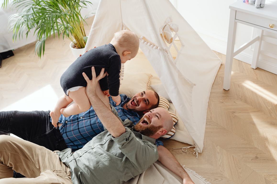 Zwei Männer, die mit ihrem Kind vor einem Zelt spielen.