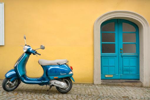 Ein blaues Moped, das vor einem Haus steht. Das Moped ist über eine Mopedversicherung abgesichert, die über die Versicherungs-App Sophia abgeschlossen wurde.