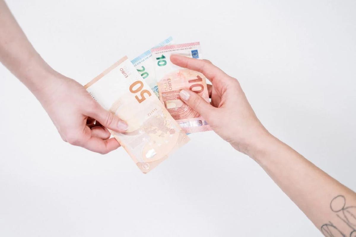 Eine Hand reicht einer anderen Geld. Ein Symbolbild für Krankengeld-, Krankenhaustagegeld-Versicherung und Ersatztagegeld der privaten Krankenversicherung in Österreich.