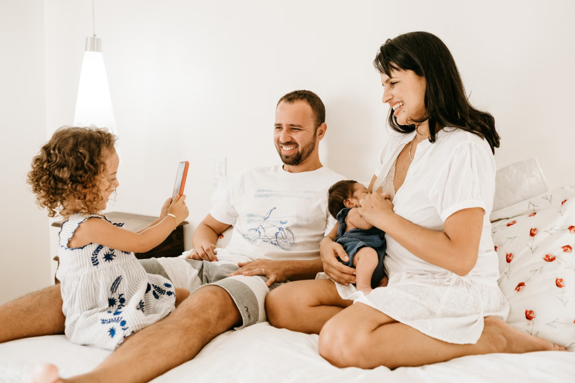 Familie mit zwei Kindern sitzt gemeinsam im Bett. Symbolbild für familiäre Geborgenheit und private Absicherung mit der Muki Krankenversicherung in Österreich.