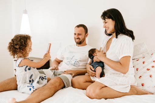 Familie mit zwei Kindern sitzt gemeinsam im Bett. Symbolbild für familiäre Geborgenheit und private Absicherung mit der Muki Krankenversicherung in Österreich.
