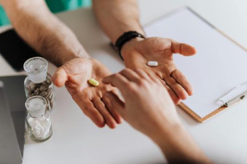 Das Foto symbolisiert den Vergleich von privaten Krankenversicherungen: Zwei geöffnete Hände bieten einer Person zwei verschiedene Pillen an, die dritte Hand greift nach einer der Optionen.