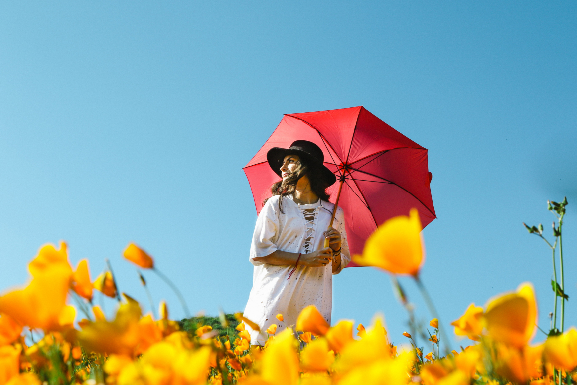 Eine Frau mit einem roten Regenschirm steht in einem Feld voller gelber Blumen.