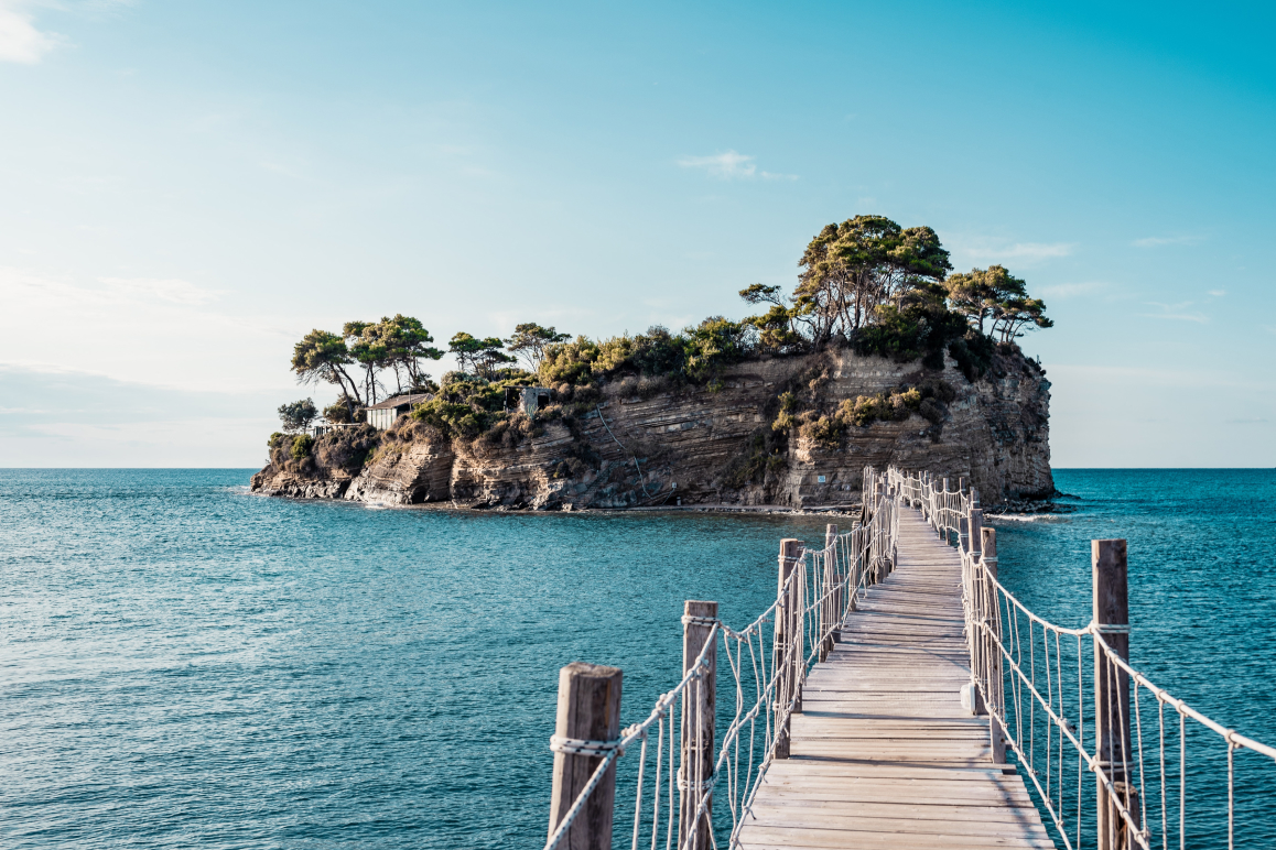 Eine braune Holzbrücke über blauem Meer unter blauem Himmel.