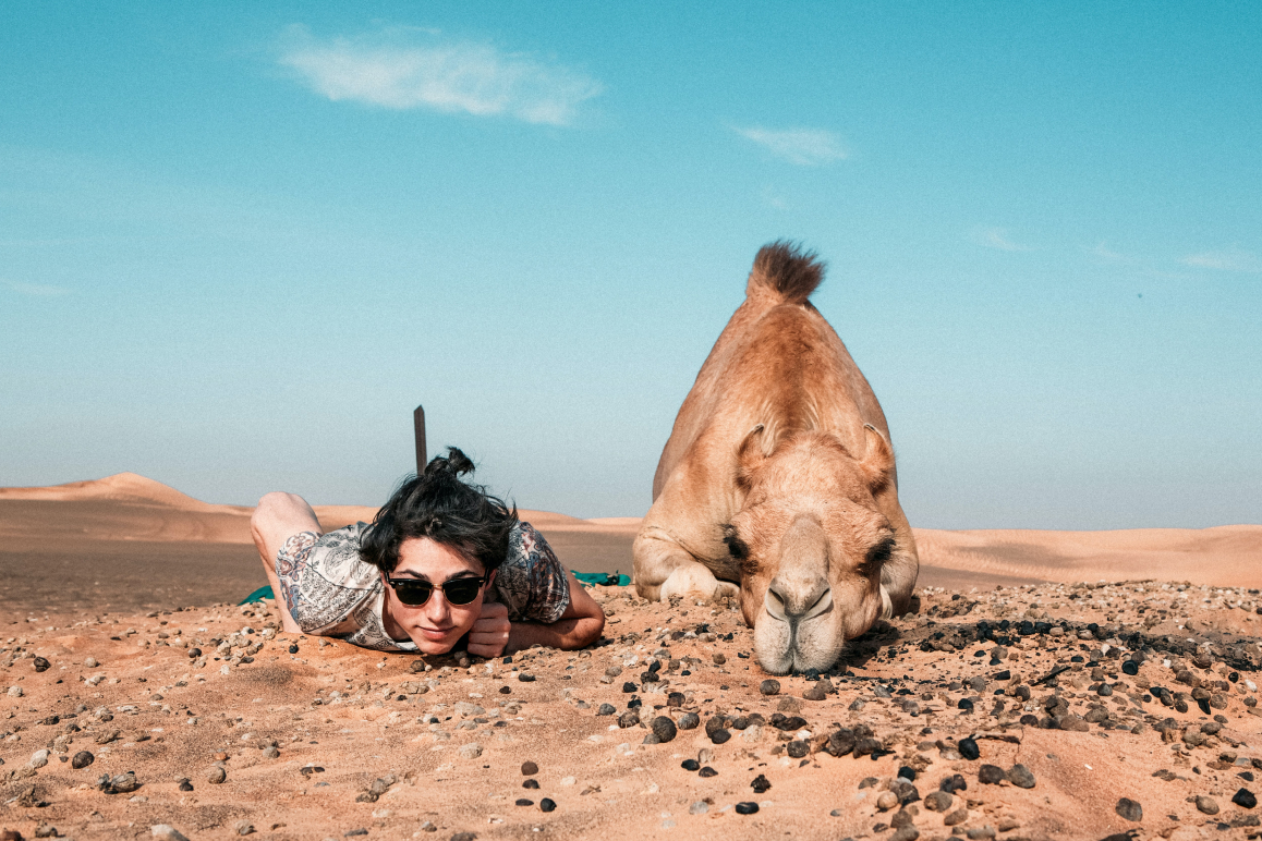 Ein Mann und ein Kamel liegen am Boden in der Wüste.