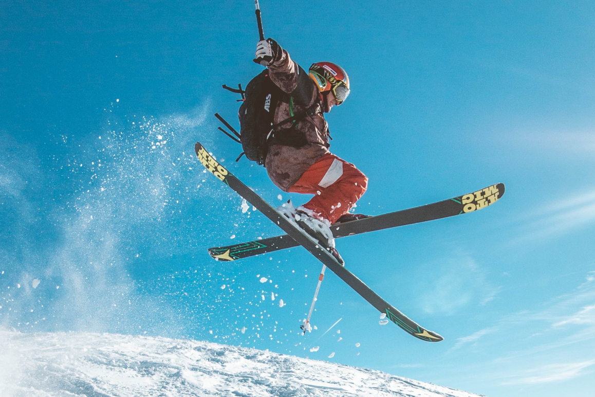 Ein Skifahrer der über einen Sprung gefahren ist und in der Luft einen Trick macht.