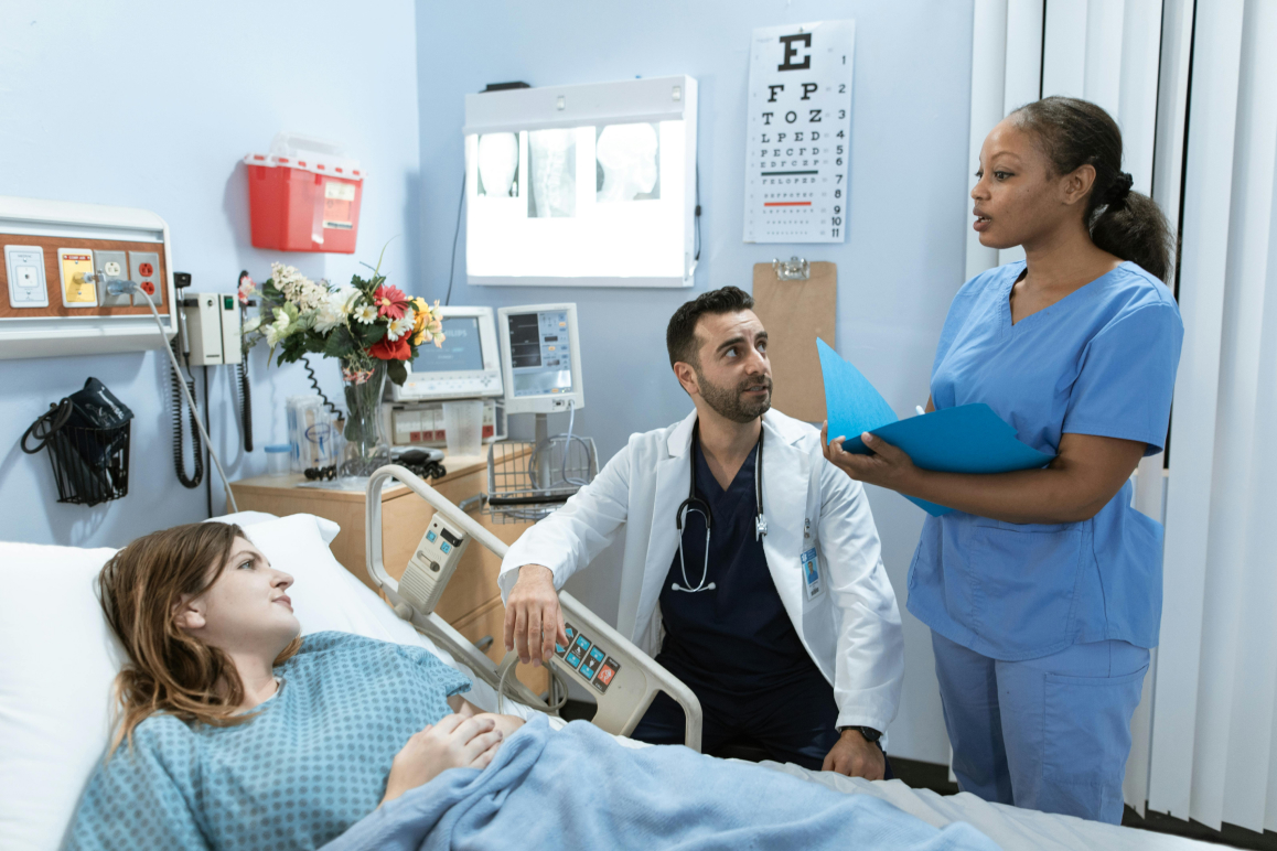 Eine Frau liegt im Krankenhausbett und wird von einem Arzt und einer Pflegerin umsorgt. Weil sie eine Sonderklasse-Versicherung hat, ist es ein Einzelzimmer.