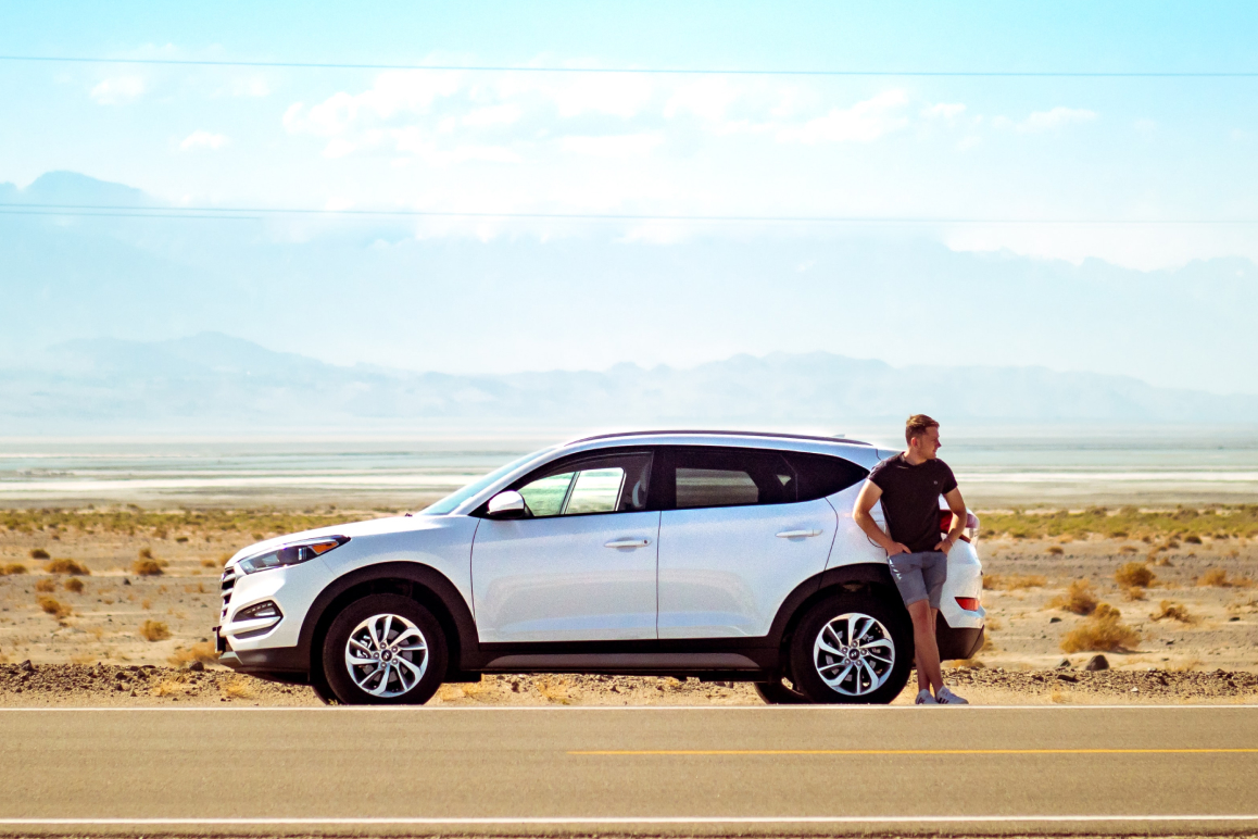 Ein Mann steht vor einem weißen Auto in der Wüste.
