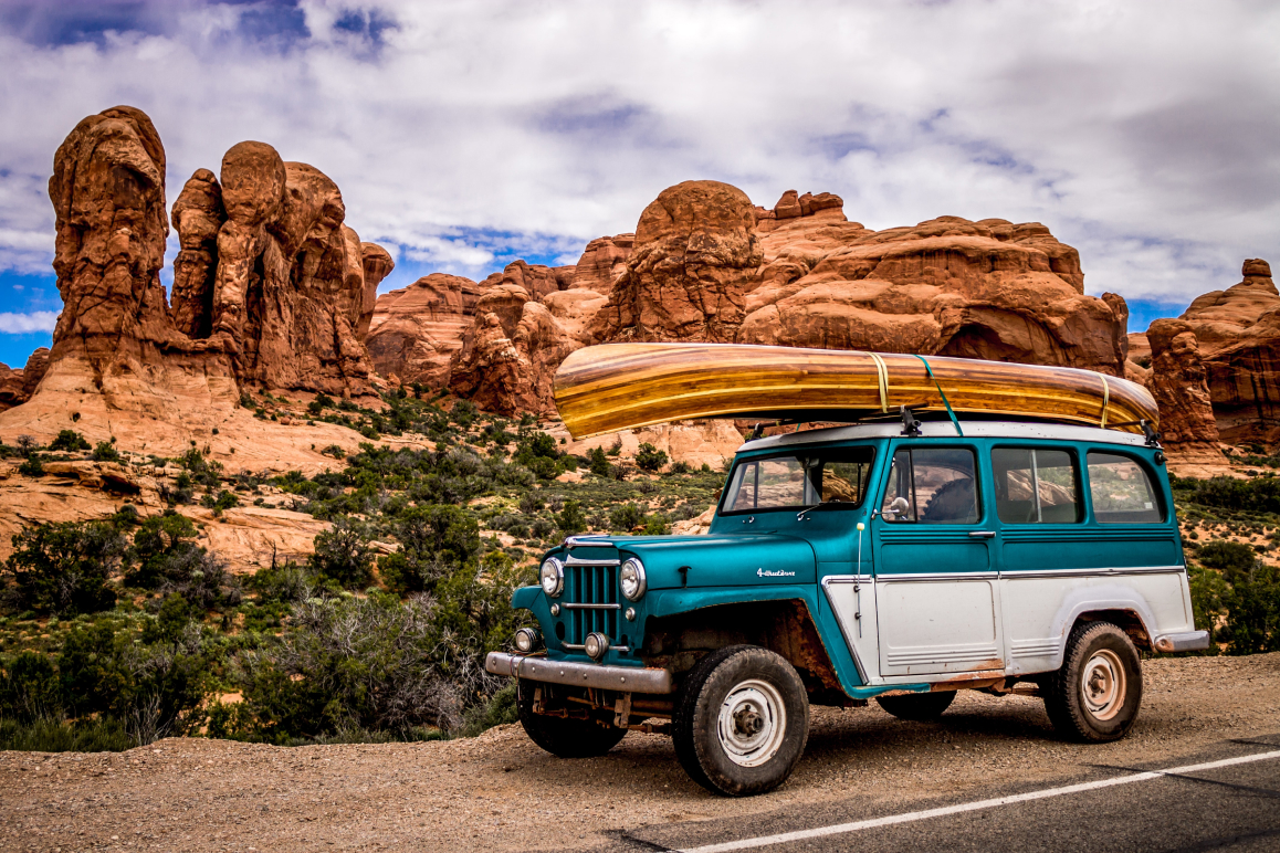 Ein Retro-Jeep mit Kanu auf dem Dach, das eine prima Autoversicherung hat und dessen Fahrer Mitglied beim ÖAMTC oder ARBÖ ist.